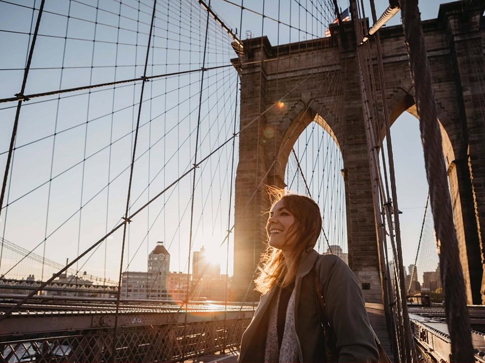 Frau steht auf der Brooklyn Bridge und genießt den Sonnenaufgang 