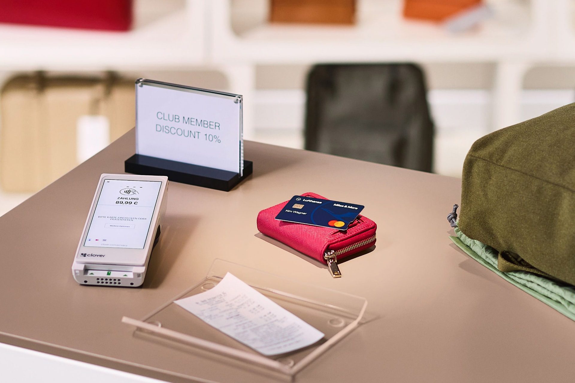 Die Miles & More Blue Credit Card liegt auf einer Geldbörse neben einem City-Rucksack auf einem Verkaufstresen. 