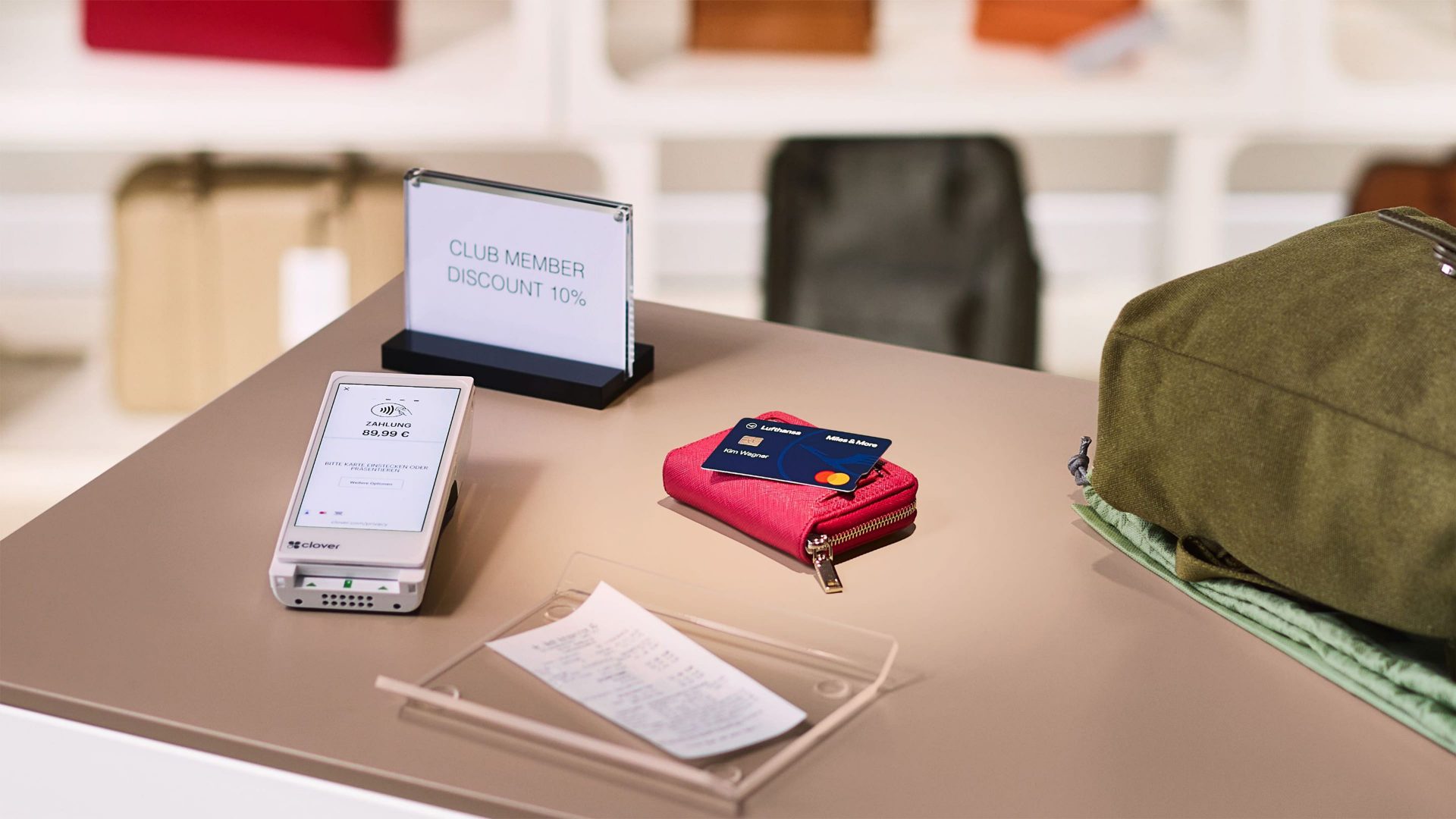 Die Miles & More Blue Credit Card liegt auf einer Geldbörse neben einem City-Rucksack auf einem Verkaufstresen. 