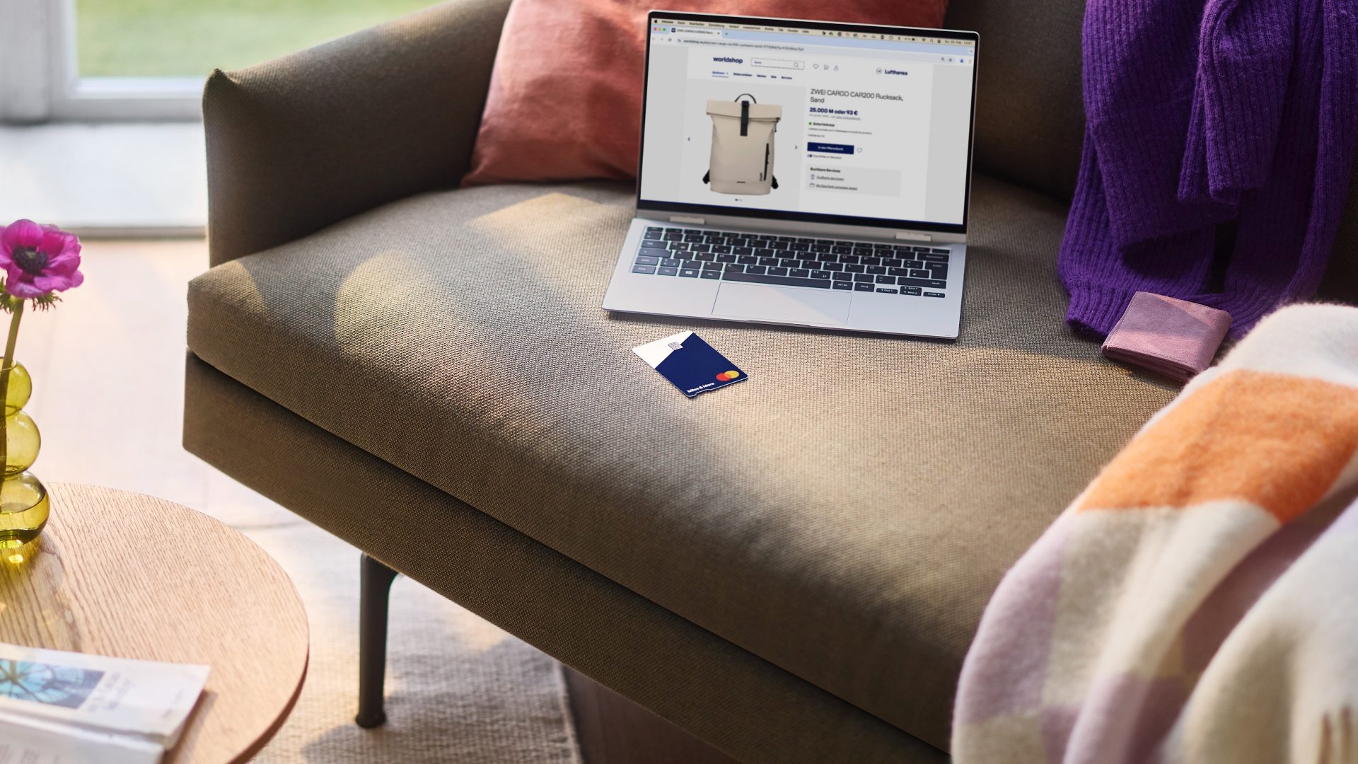 Laptop mit Rucksack Webseite und Miles & More MyFlex Credit Card auf Sofa vor Fenster
