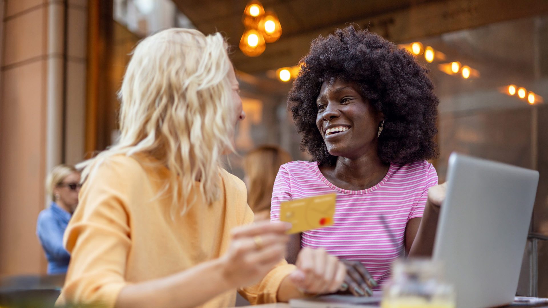 Zwei Frauen sitzen vor Laptop im Cafe mit Gold Credit Card in der Hand 