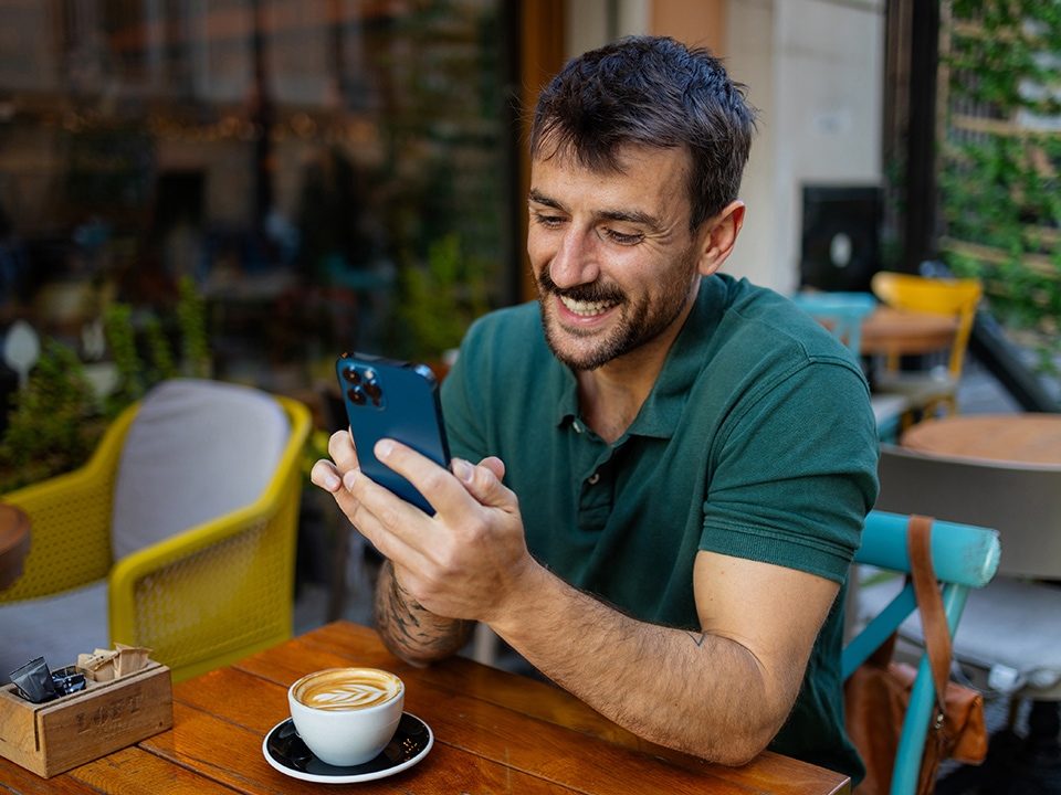 Mann sitzt im Cafe und schaut lächelnd auf sein Smartphone 