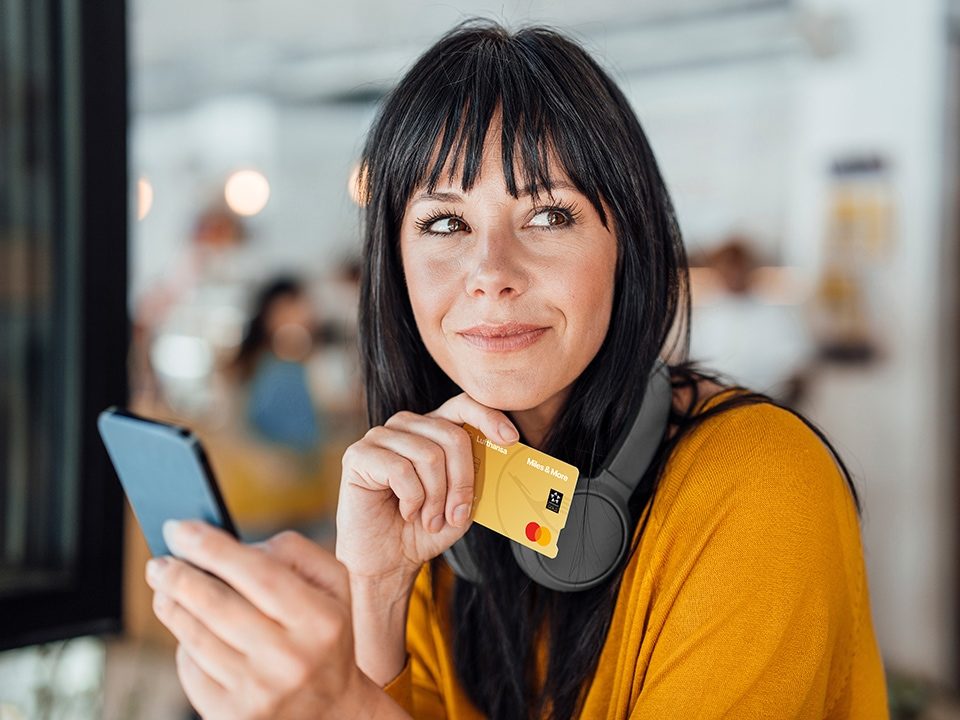 Frau mit Kopfhörern hält Handy und Gold Credit Card in der Hand und lächelt zur Seite
