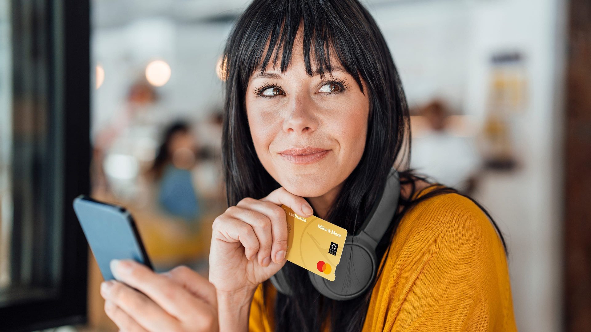  Frau mit Kopfhörern hält Handy und Gold Credit Card in der Hand und lächelt zur Seite