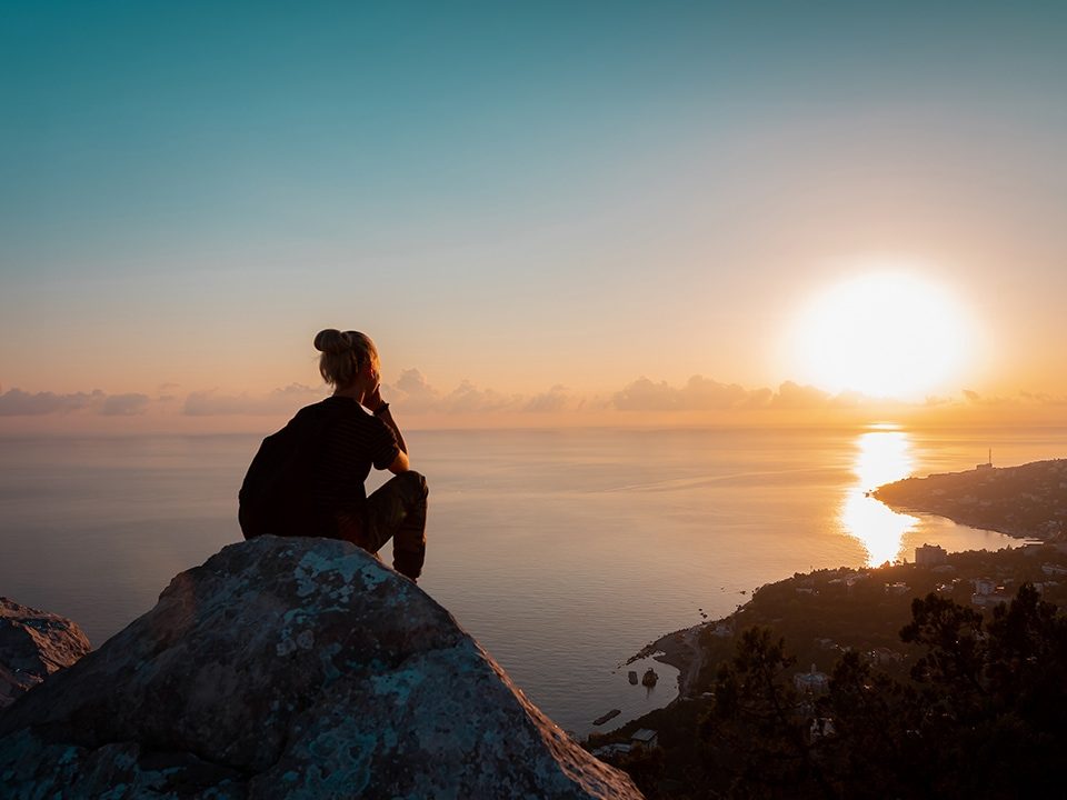 Frau sitzt auf einem Berg und schaut über das Meer während Sonnenaufgang 