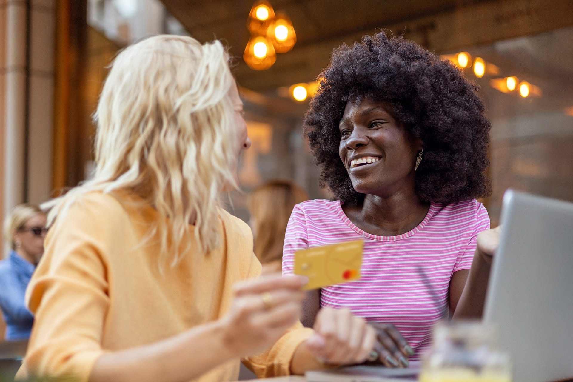 Zwei Frauen sitzen vor Laptop im Cafe mit Gold Credit Card in der Hand 
