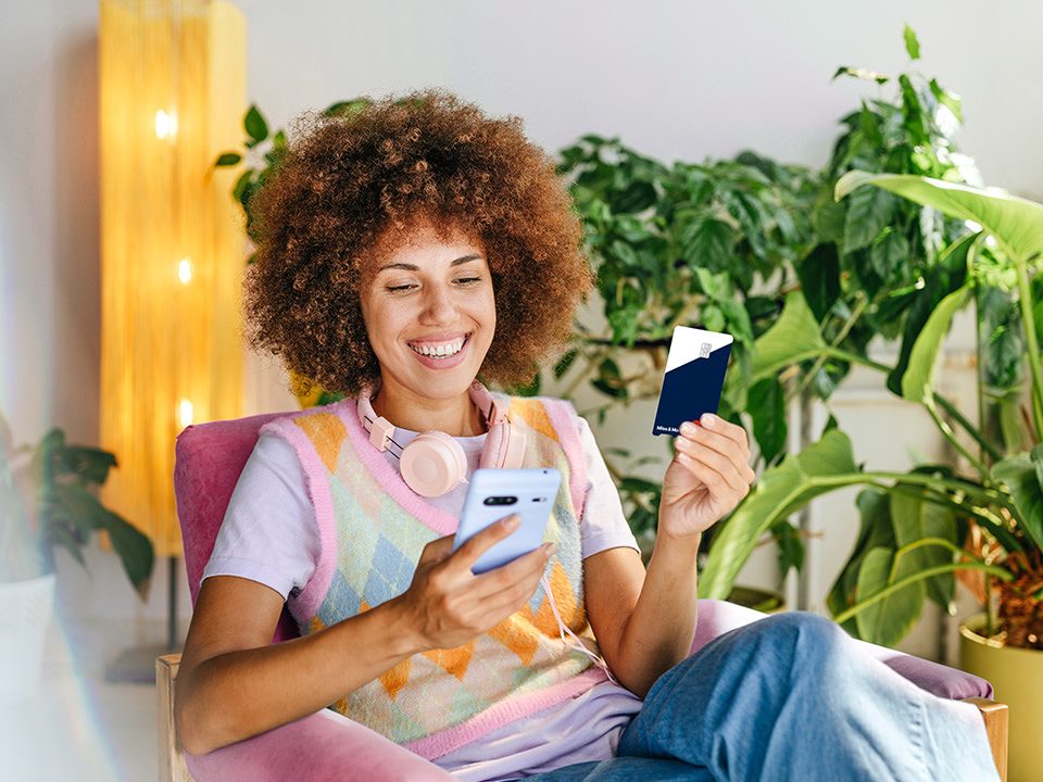 Person im Sessel mit Smartphone und Miles & More MyFlex Credit Card. 